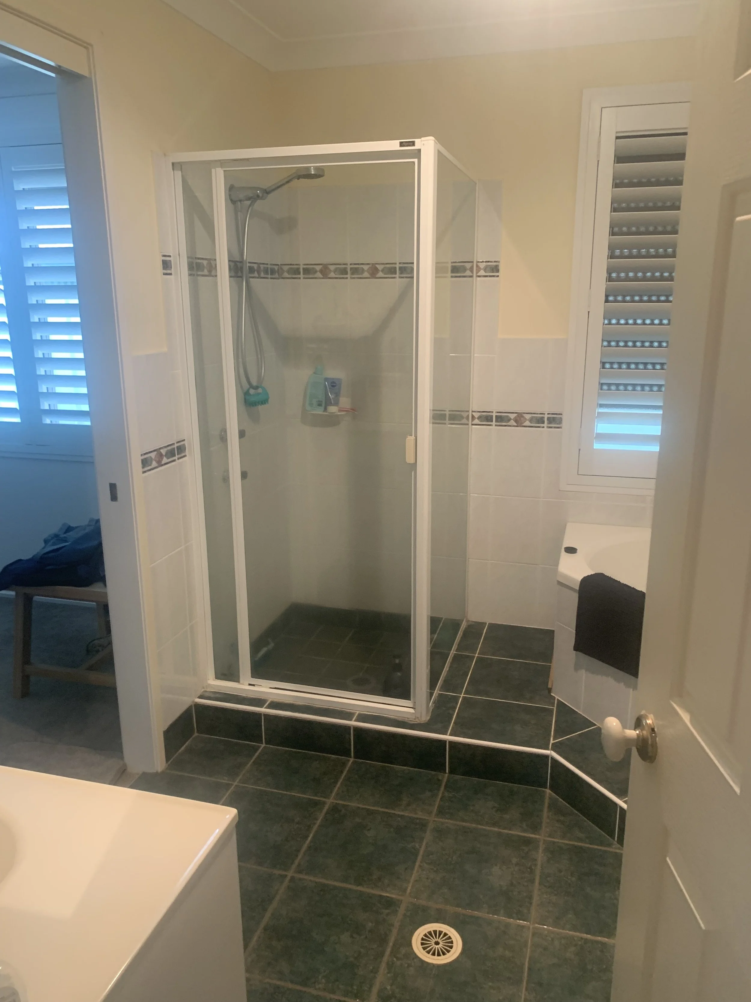Bathroom with a shower stall, window with blinds, and black tiled floor.