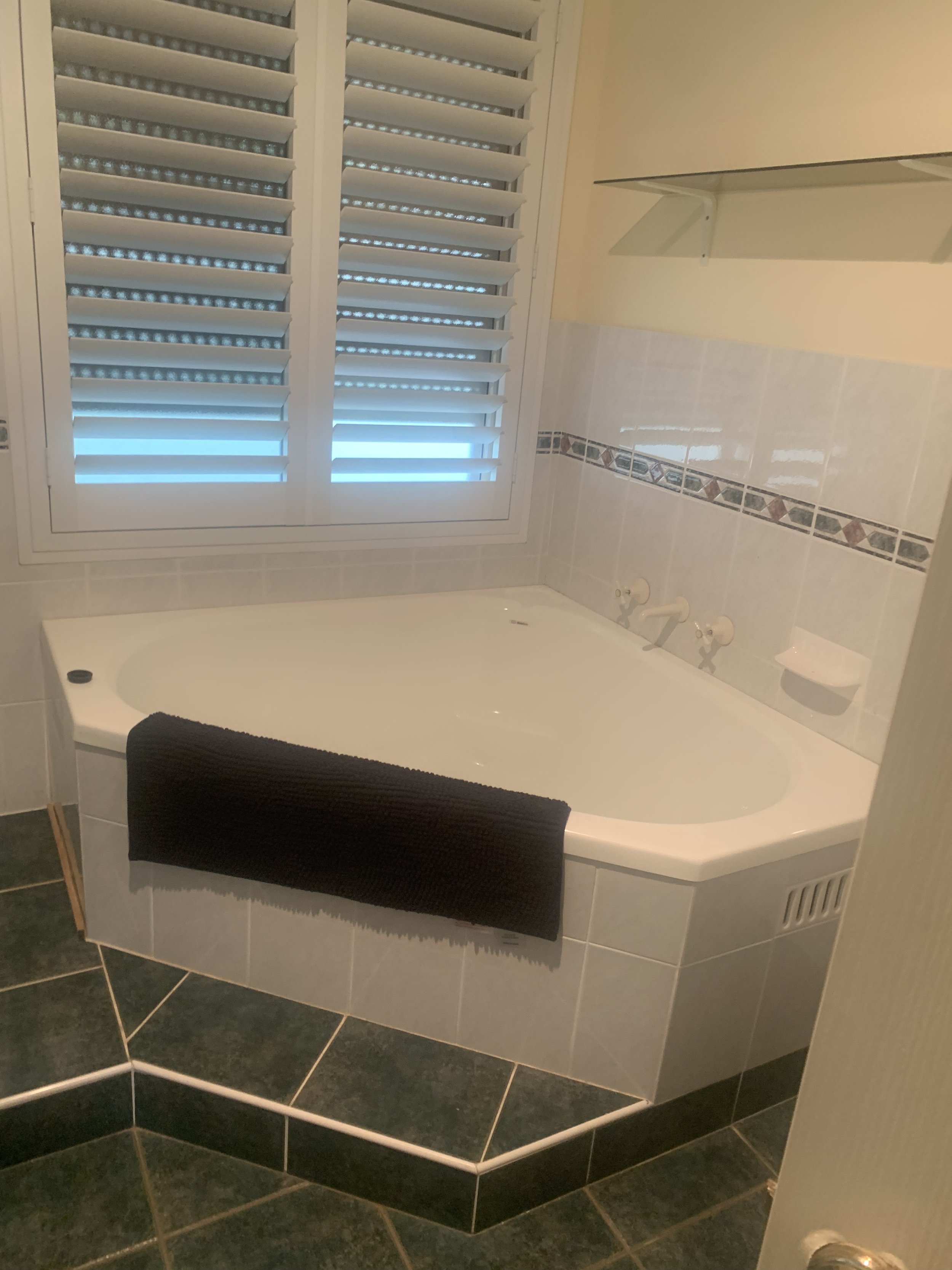 Bathroom with a bathtub, black towel, window with white shutters, tiled walls and floor.