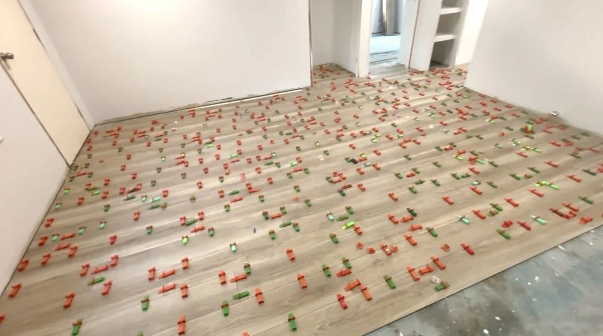 A hardwood floor being installed in a room, with numerous orange and green tile spacers scattered across the surface.