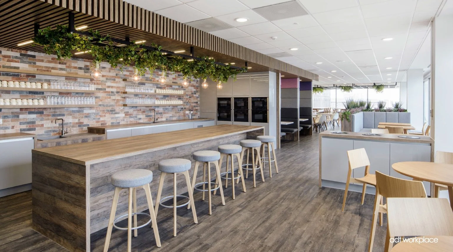 Modern cafe with wooden tables, bar stools, brick wall, hanging lights, and indoor plants.