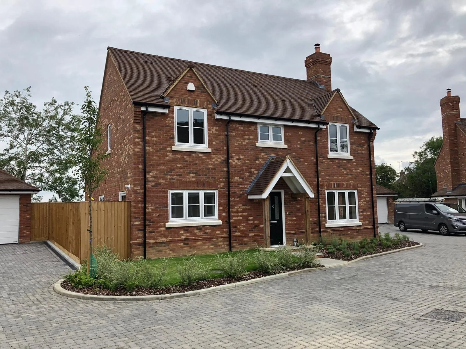 New brick house with white trim, small front porch, pitched roof, and a gravel driveway, under cloudy sky.