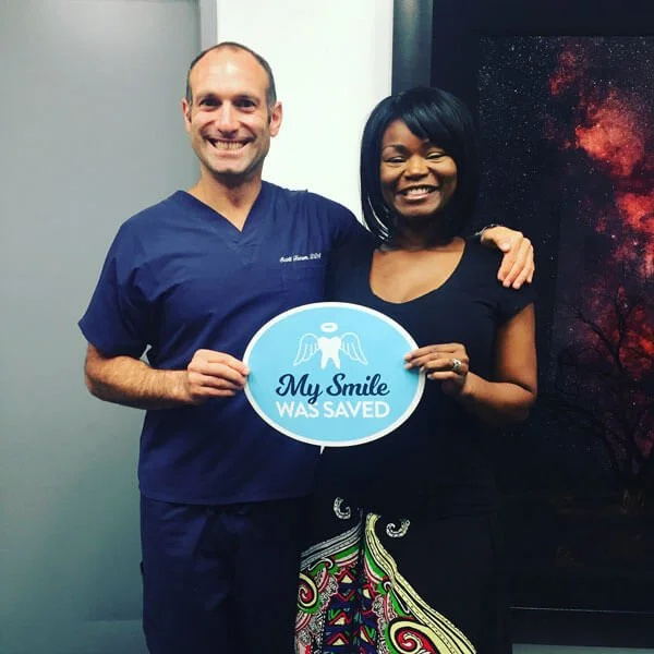 dr. scott froum in nyc and a happy patient holding a sign that says "My smile was saved"