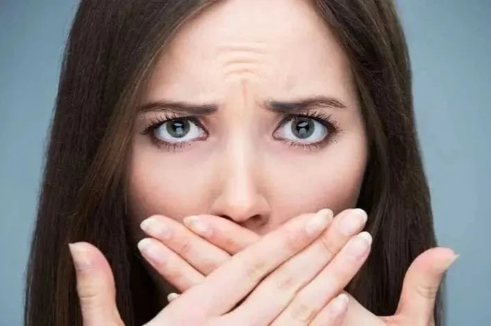 woman with brown hair holding both hands over bad breath mouth
