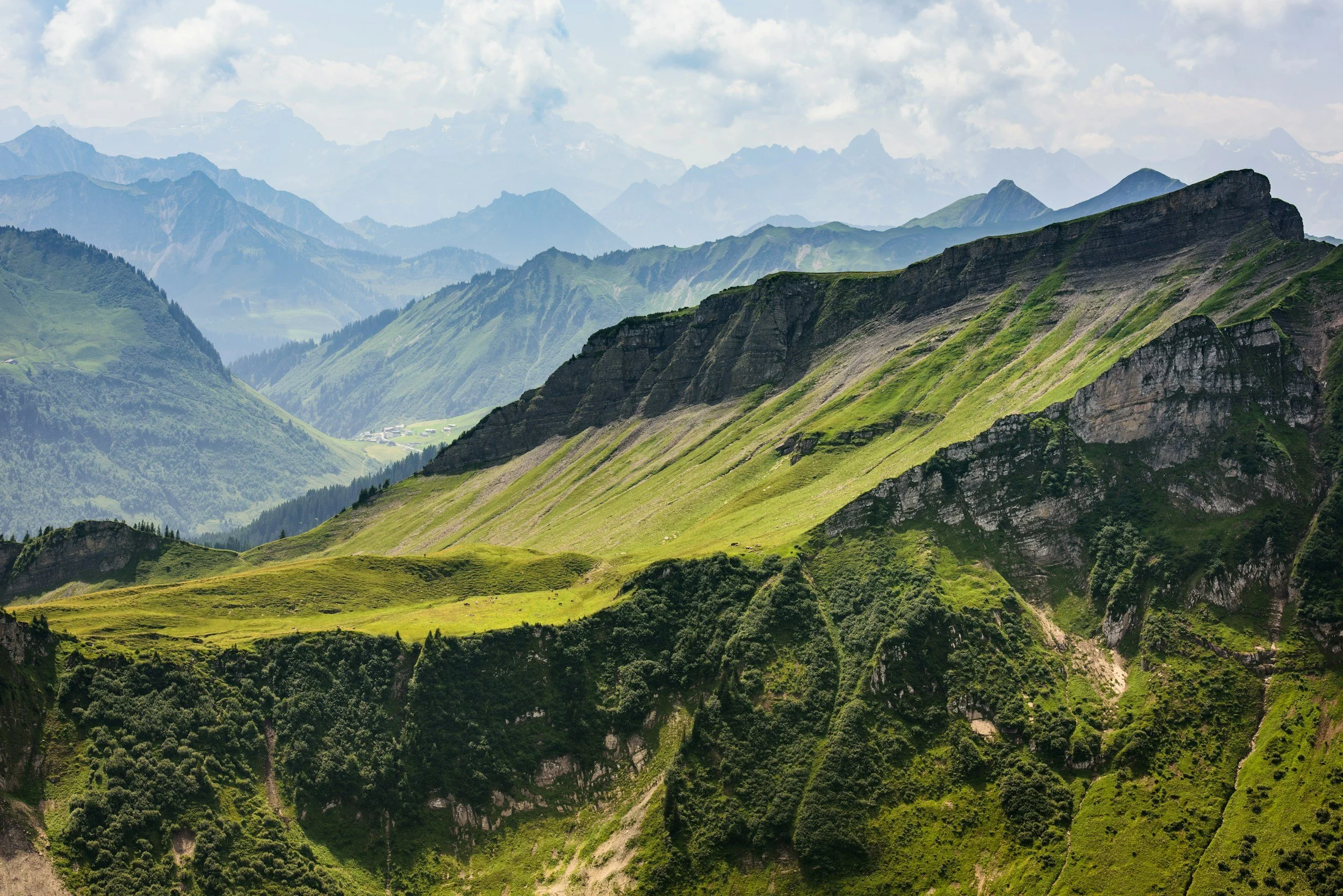 Scenic view of green rolling hills and rugged mountains under a partly cloudy sky.