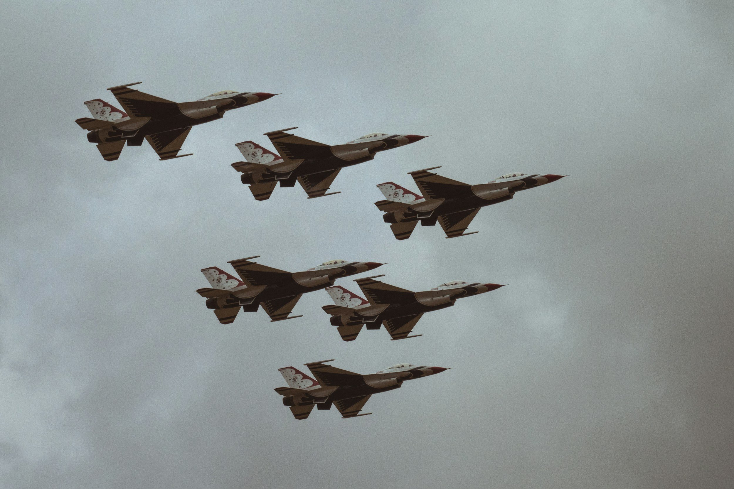 Six fighter jets flying in a tight formation against a cloudy sky.