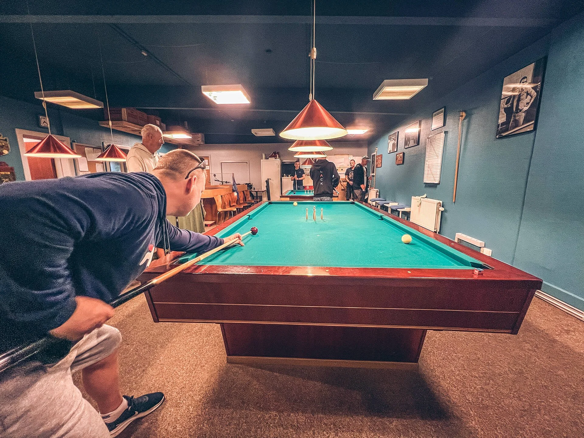 En ung mand spiller billiard i et hyggelig billiardlokale med blå vægge og billeder på væggene.