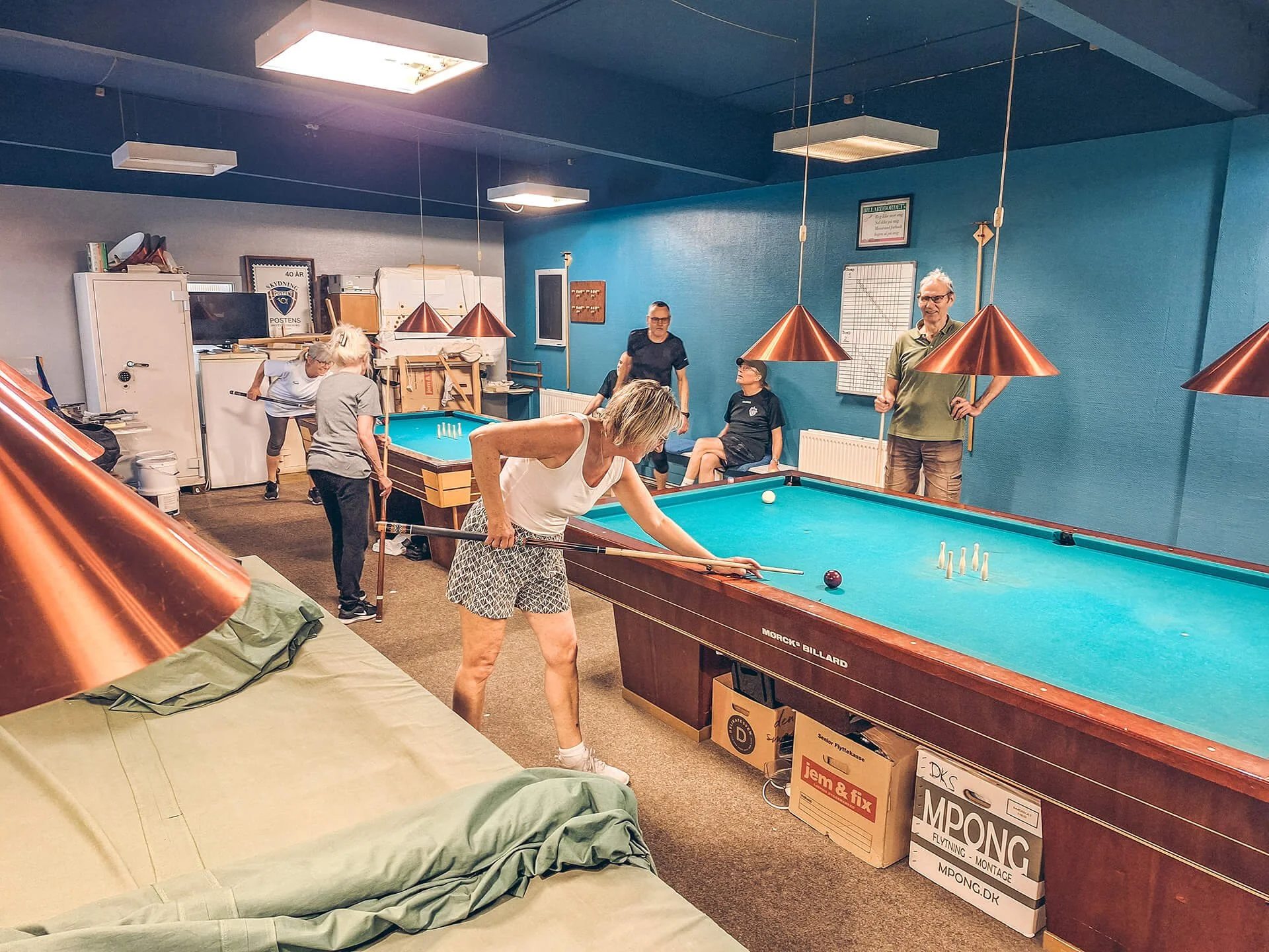 Person, der spiller billard i et rum med flere personer, some sidder og observerer spillet.