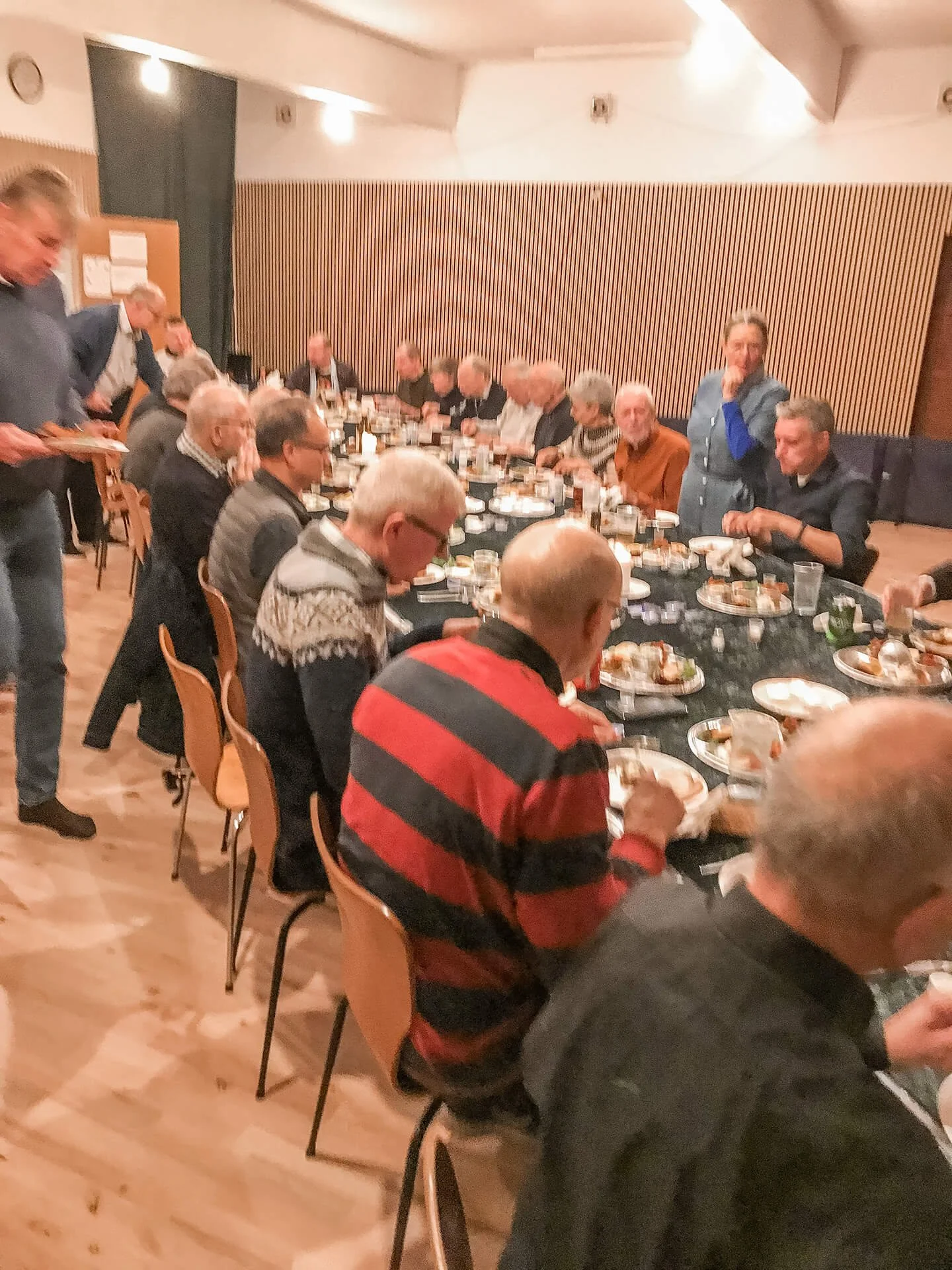 Mennesker sidder ved et langt bord og spiser i et festlokale.