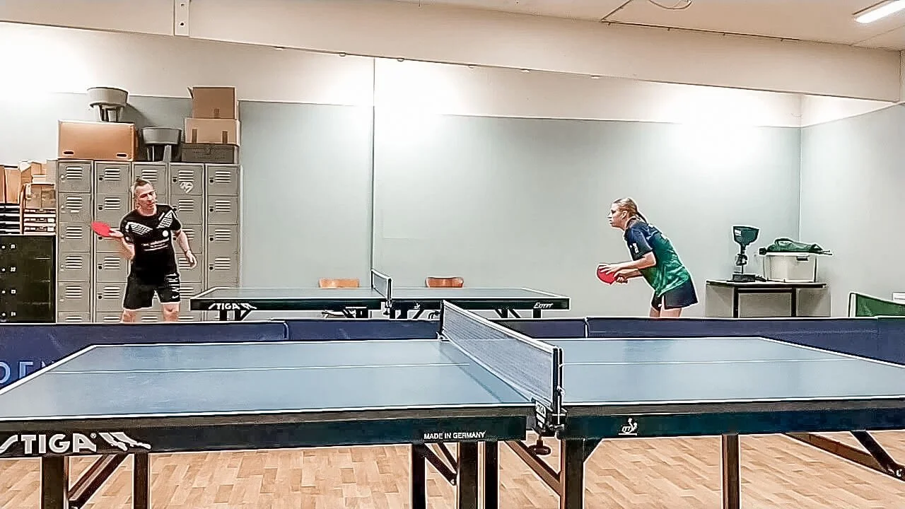 To personer spiller bordtennis i et træningslokale.