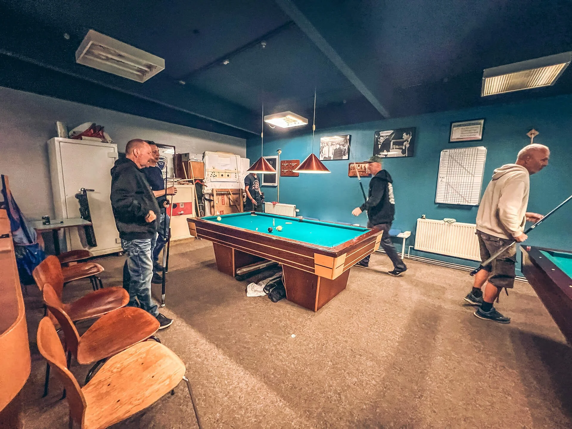 Mænd spiller billard i et billiardrum med billeder på væggen