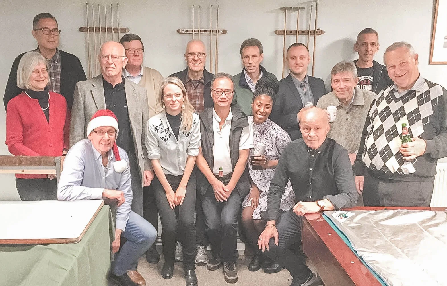 Gruppe af mennesker, der fejrer jul med julehats og drikkevarer i et rum med poolbats verden bagved.