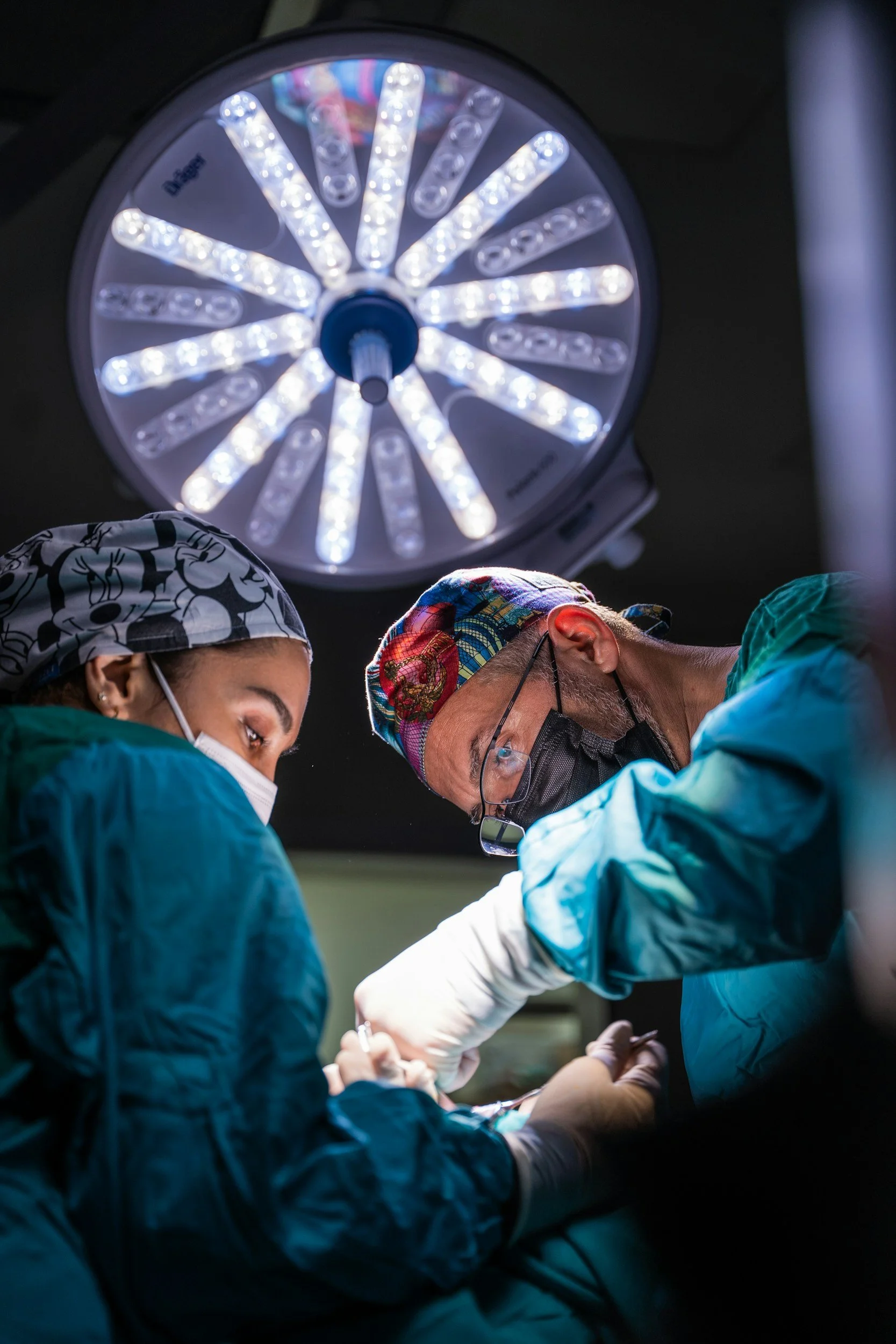 Two surgeons performing an operation in an operating room with a large surgical light overhead.