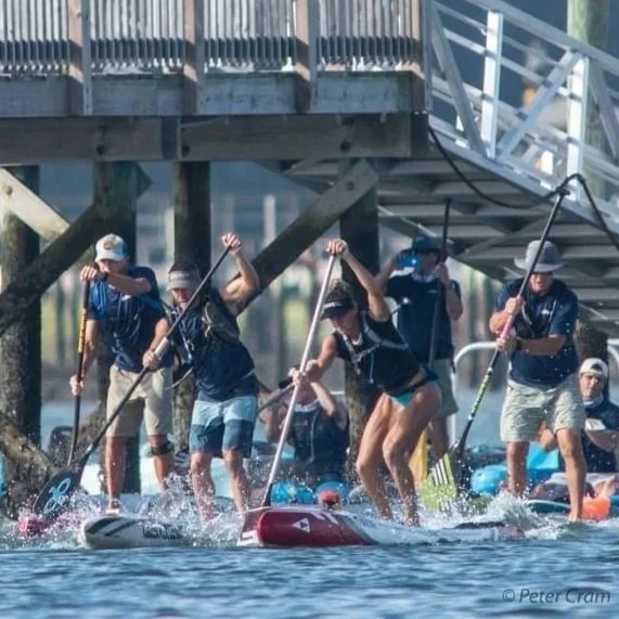 Several people paddleboarding in a waterway near a wooden dock and stairs, enjoying a sunny day.