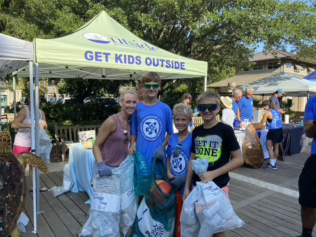 Four kids and an adult at an outdoor event, holding bags, under a tent with a sign that says 'Get Kids Outside', promoting outdoor activities for children.