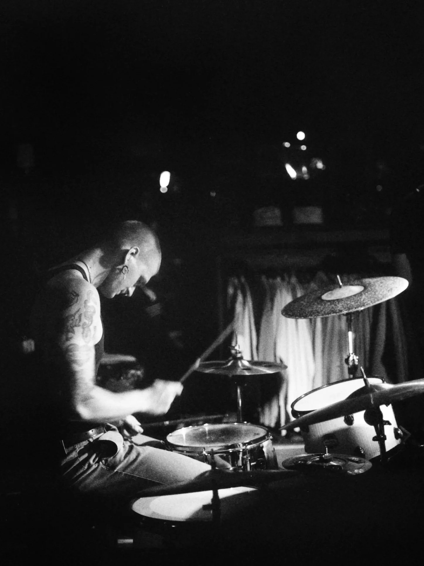 A person playing the drums in a dark setting, with a focus on the drum set and drumsticks.