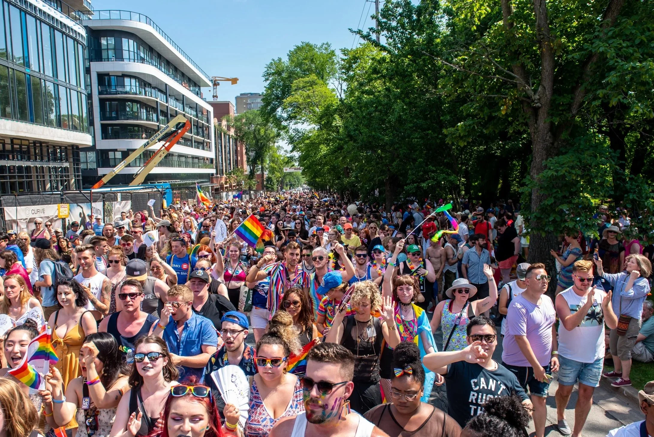 Crowd of people celebrating at a pride parade, many holding rainbow flags and wearing colorful clothing and accessories.