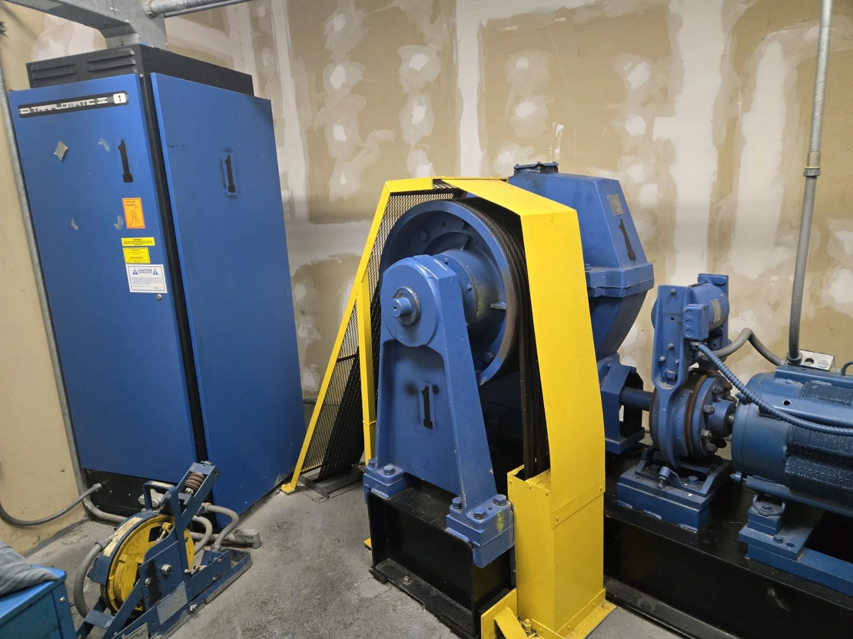 Industrial mechanical room with blue electrical cabinets and large blue motor connected to yellow safety barrier.