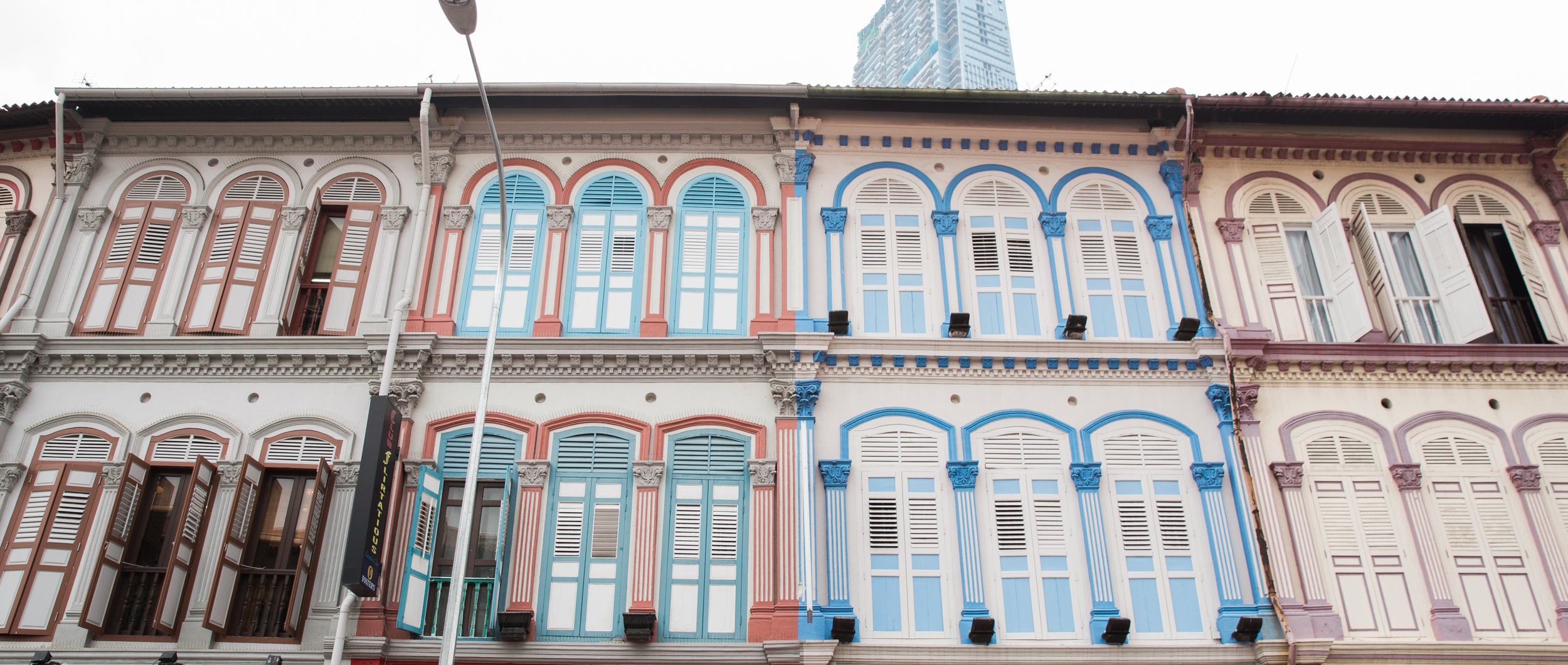 Colorful rows of colonial-style buildings with arched windows and wooden shutters in shades of pink, blue, and cream in an urban setting.
