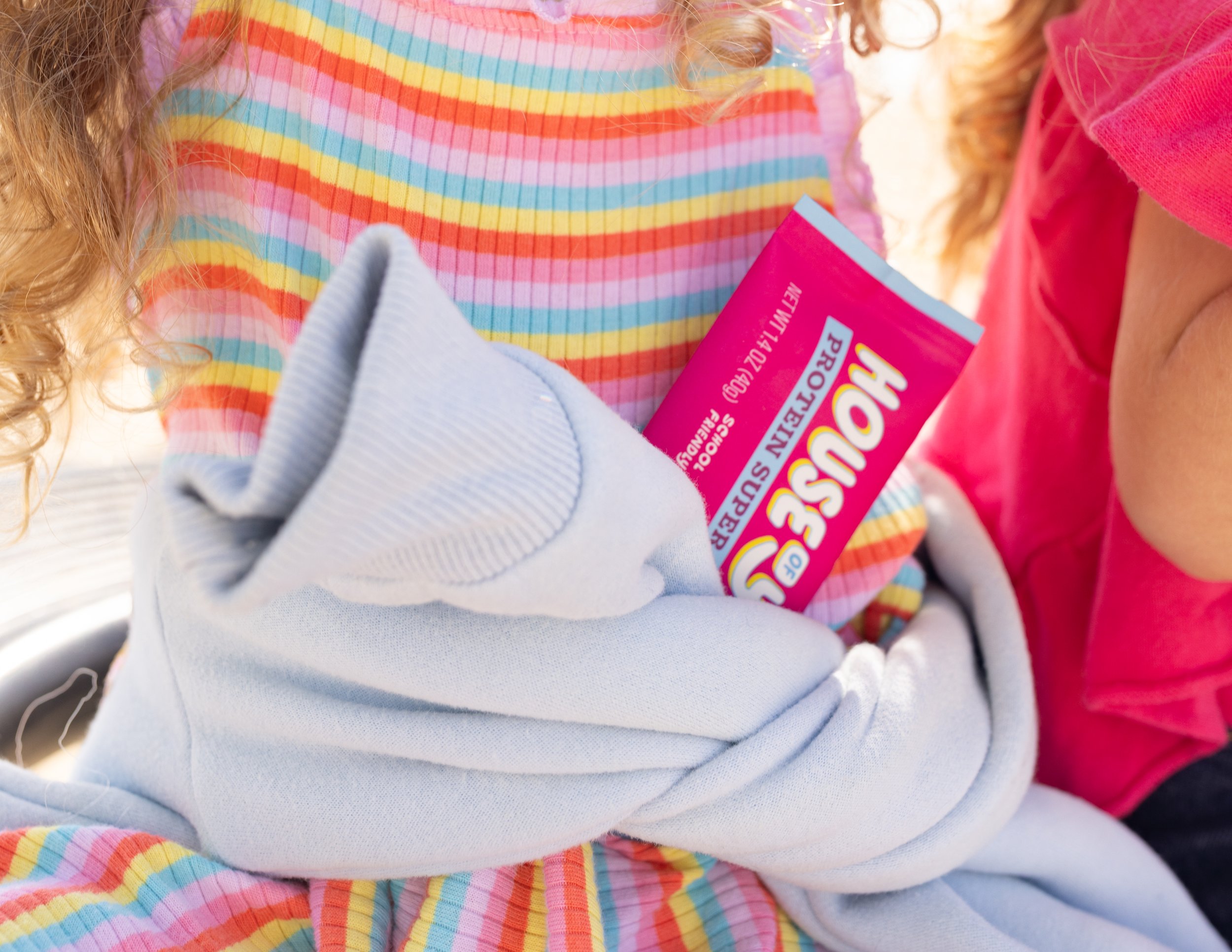 Close-up of a child's lap wearing rainbow-striped pants, a pink shirt, with someone holding a pink box of Pop-Tarts.