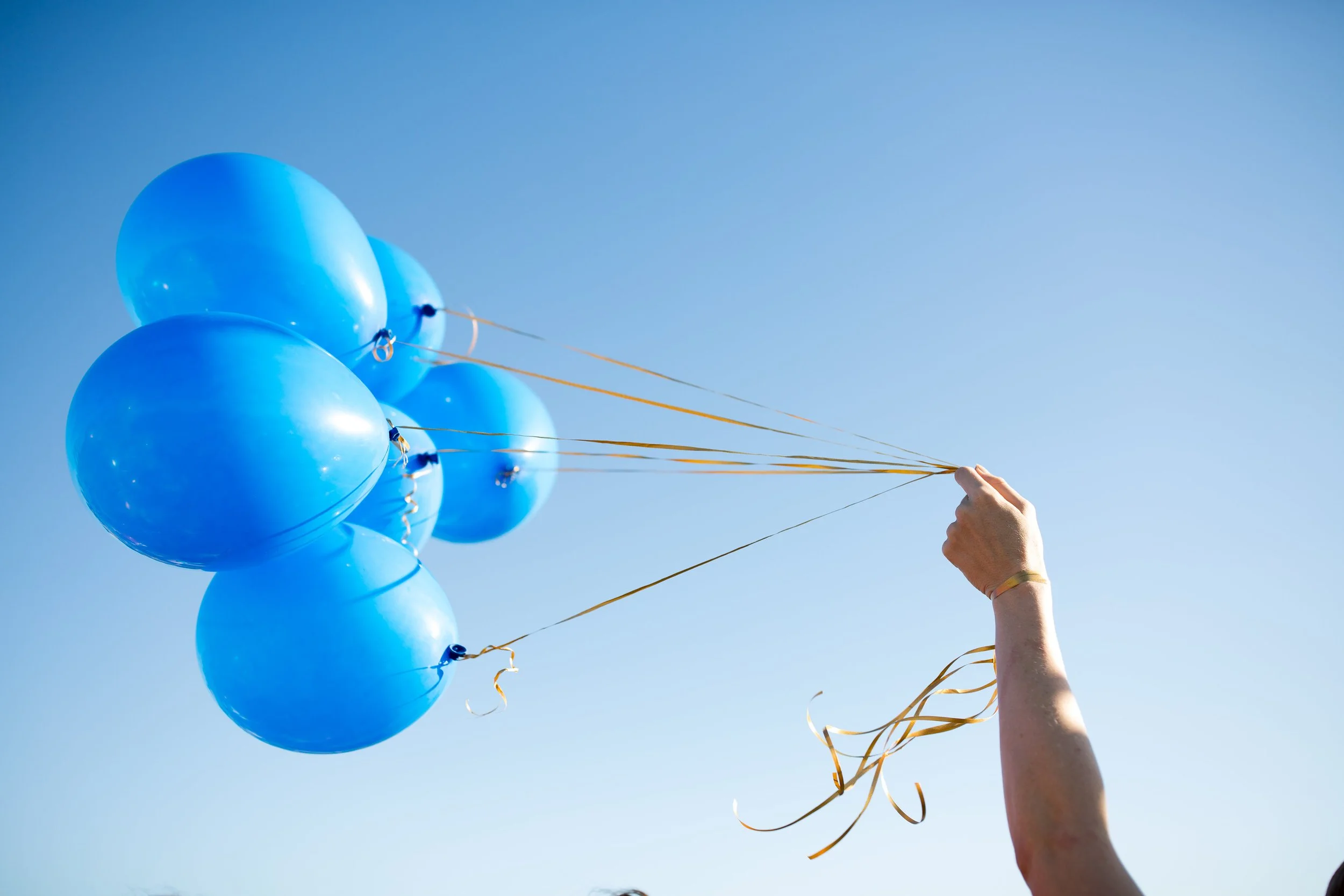 Person holding blue balloons against a clear blue sky.