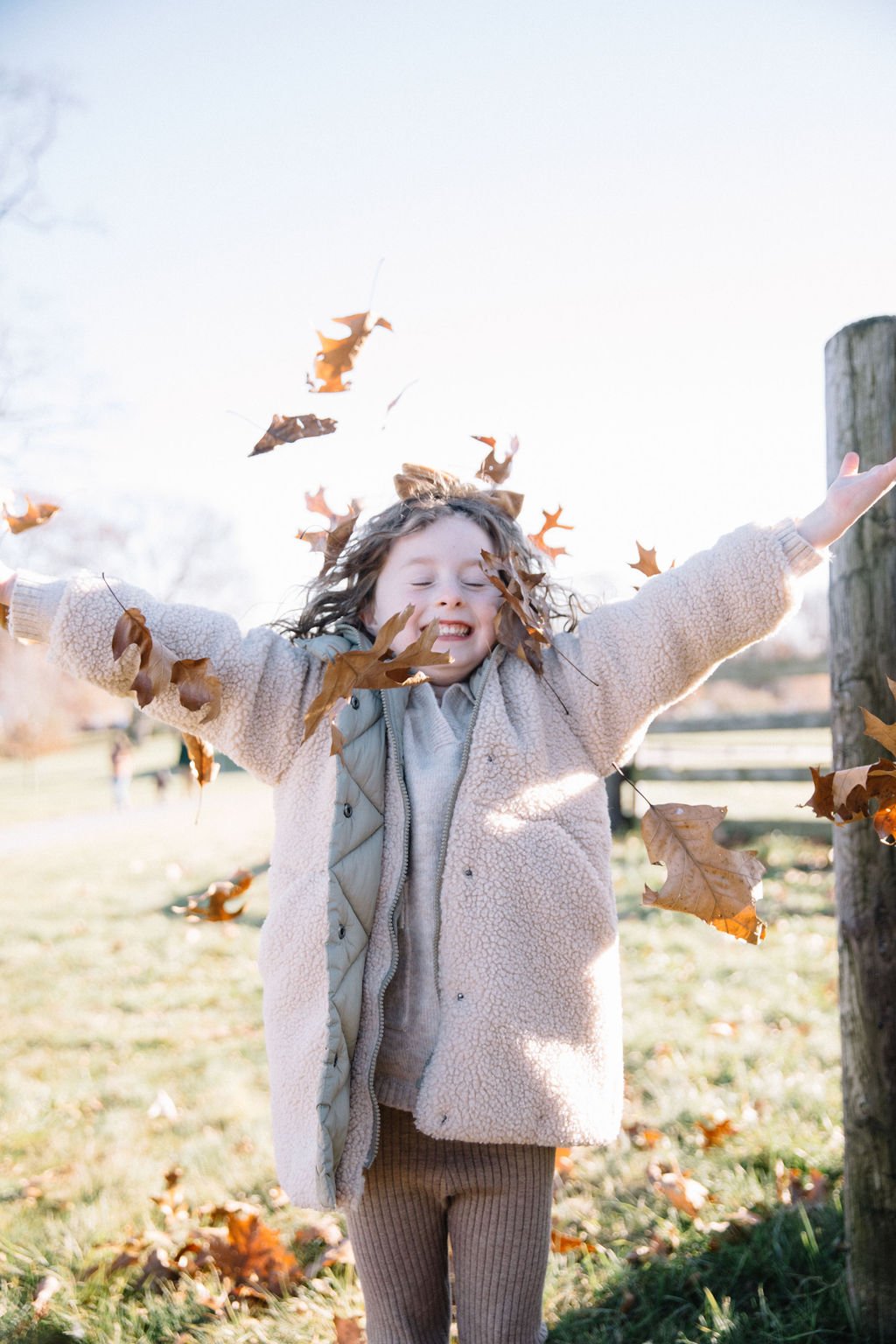 Child joyfully playing with autumn leaves outdoors, arms outstretched with a big smile.