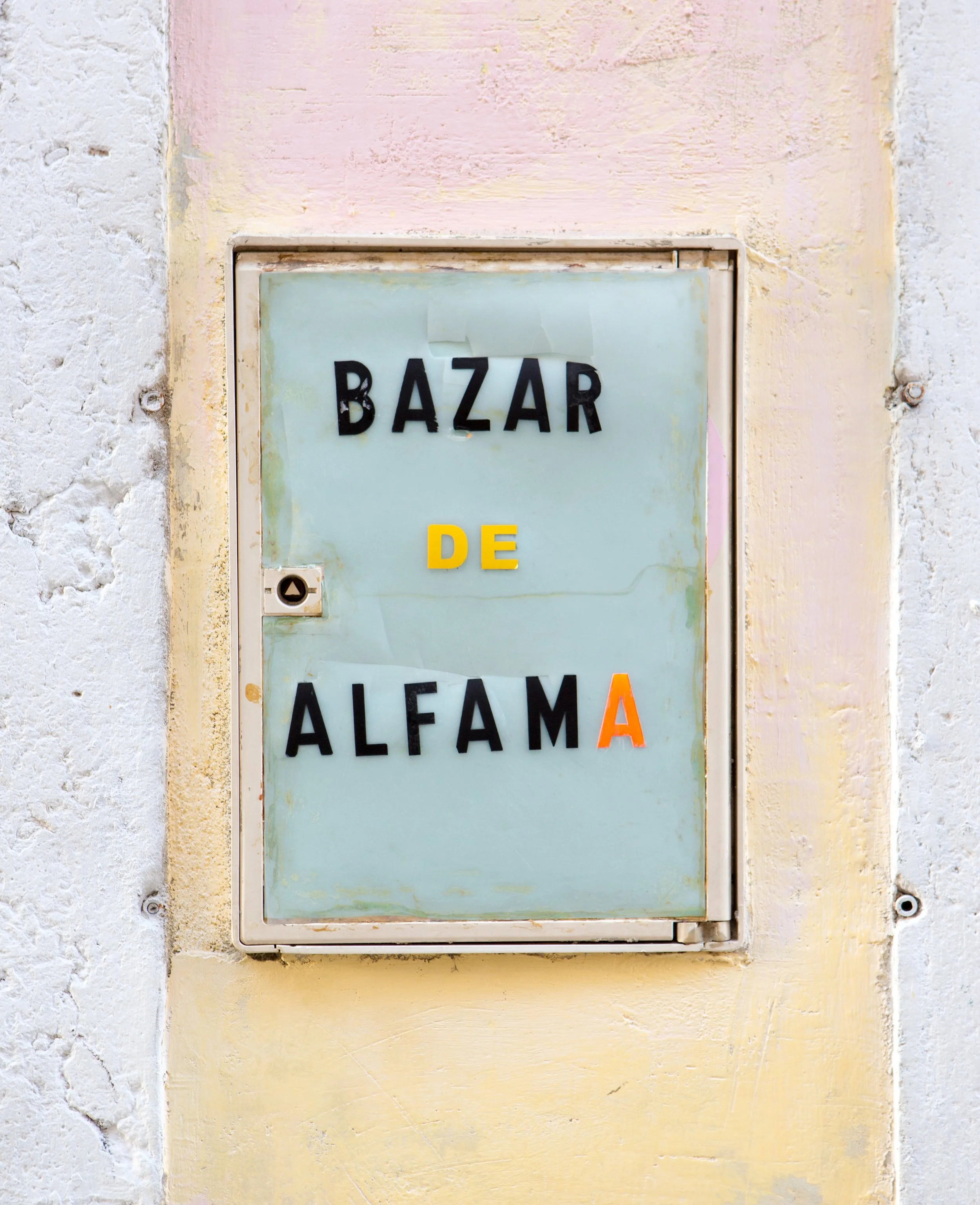 A vintage public telephone box on a textured wall. The top part says 'BAZAAR' and the bottom part says 'ALEM' with a partially visible 'A'.