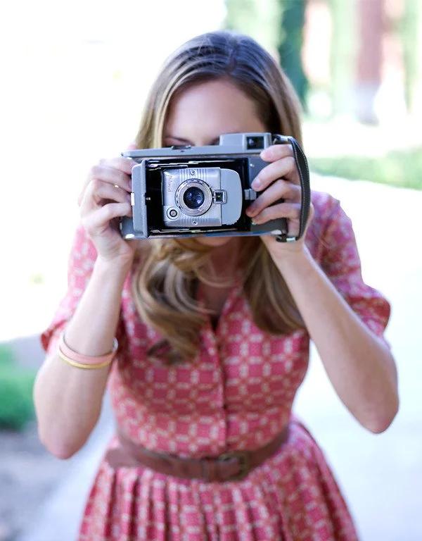 Woman holding a vintage film camera up to her face outdoors.