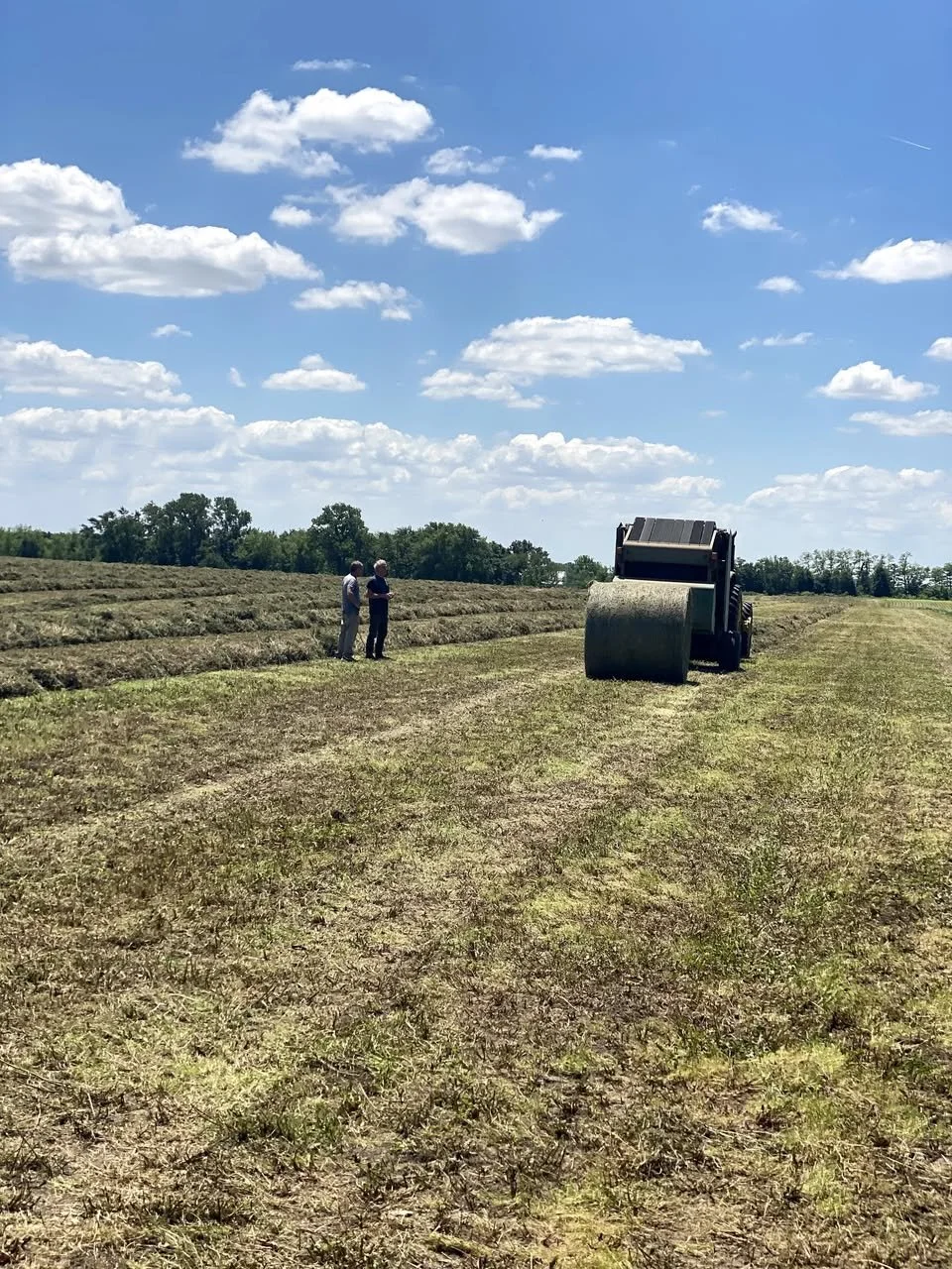 A tractor bailing hay in a field in Adams County, Illinois with Tom Neisen and another man next to it.