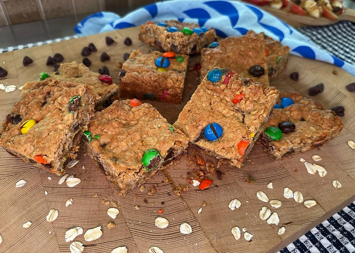A pile of monster cookie bars on a cutting board with chocolate chips and oats scattered about