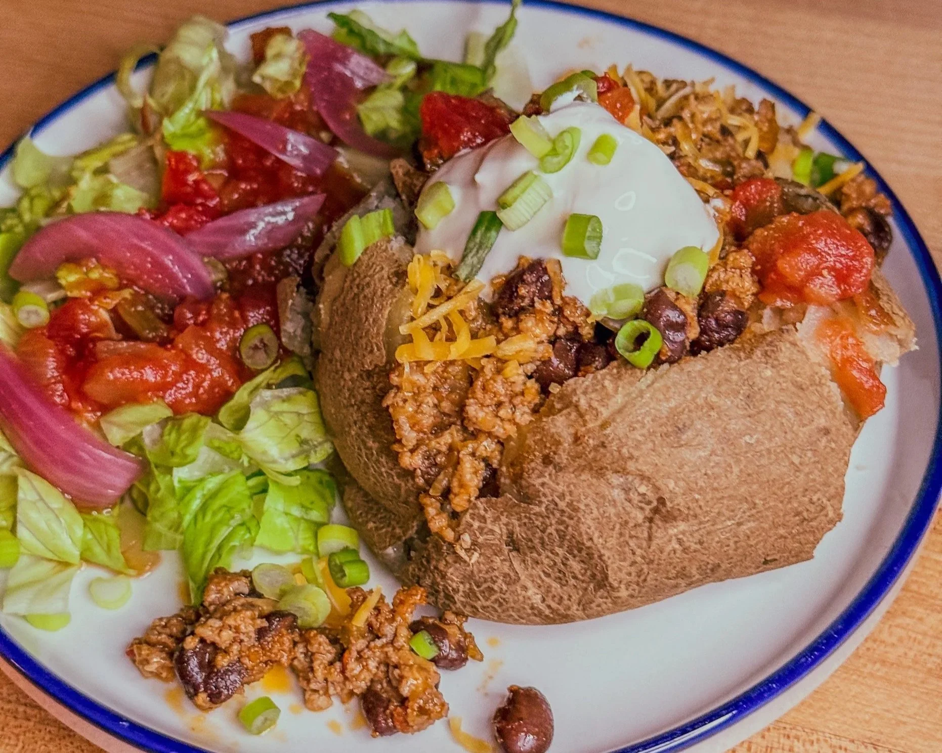 Close up view of taco stuffed baked potato and taco salad on plate by Boki's Kitchen