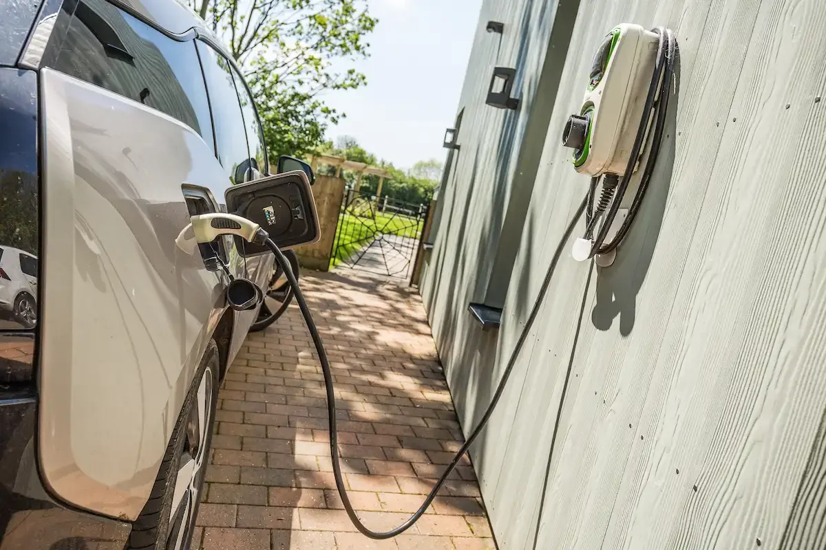 A white car parked on a drive with a close up of the car plugged into the EV charger