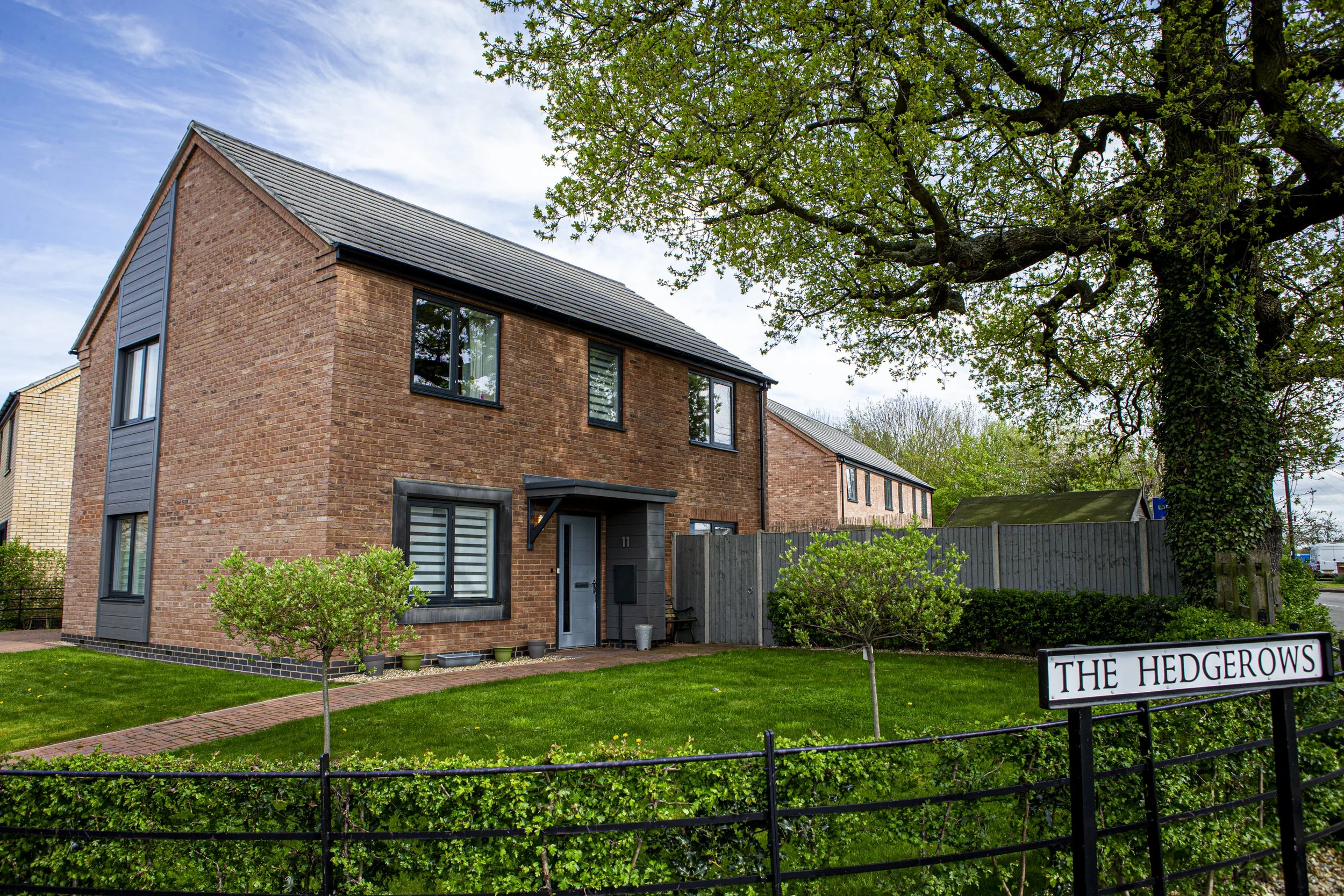 Detached house with a large front garden and black fence, sign saying 'The Hedgerows' sat at the front of the house.