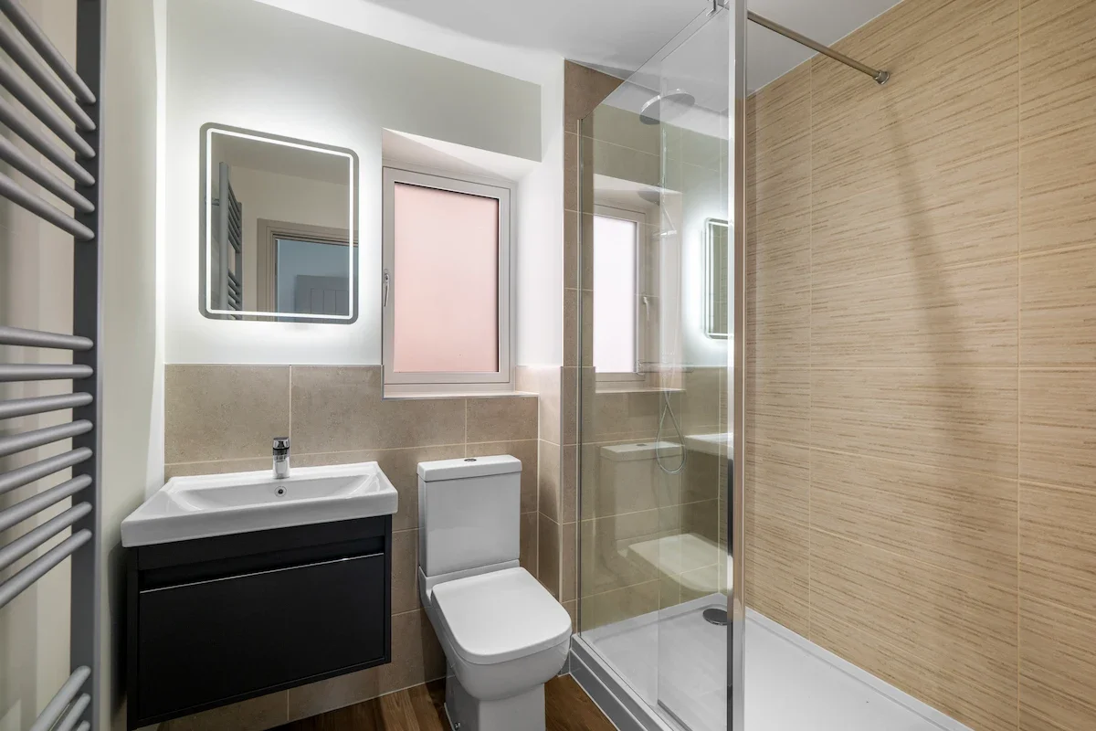 A modern bathroom with a walk in shower, toilet, mirror and towel drying rack.