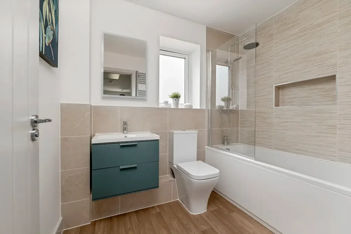 A modern bathroom with a bathtub, shower, toilet, and vanity with a mirror, decorated with neutral tones and small potted plants.