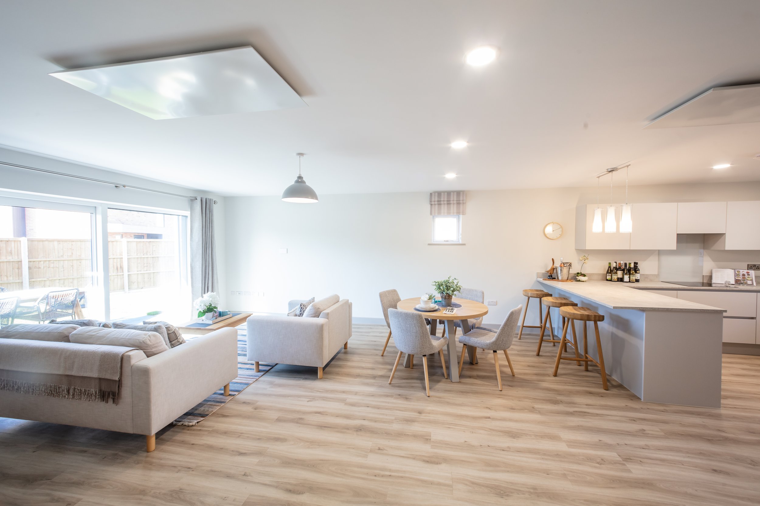 Modern open plan living area, neutral colours, two sofas, a wooden dining room table and chairs, the kitchen area has a breakfast bar