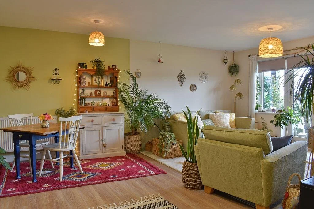 Open plan living and dining area with green sofas, table and chairs. The space includes plants and decorative features.