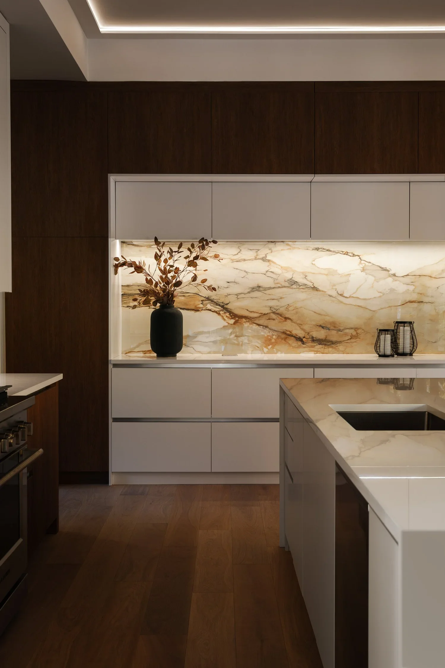 Modern kitchen with white cabinetry, a marble backsplash, a black vase with dried leaves, and a small wire basket on the countertop.