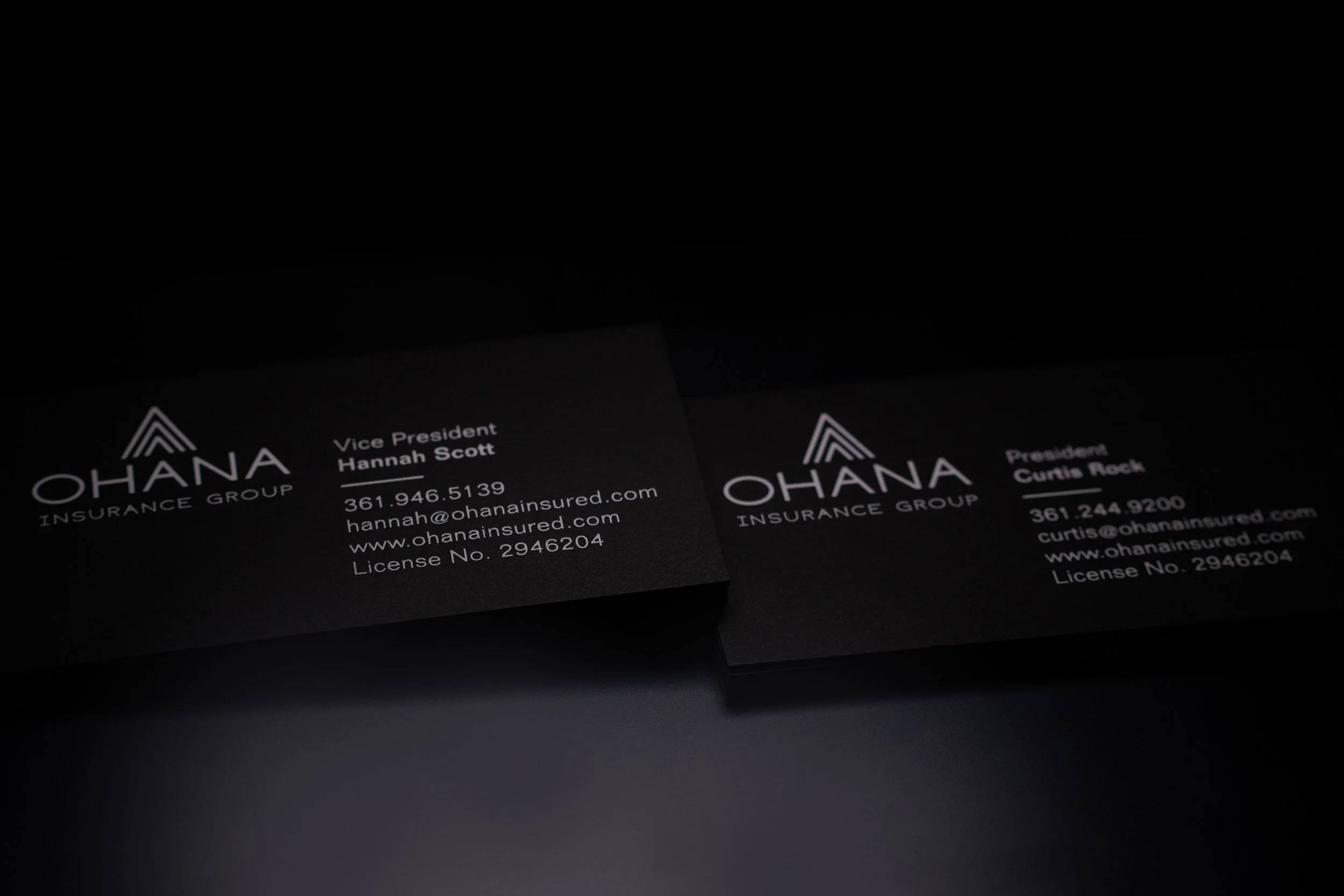 Business cards for Ohana Insurance Group, one for Vice President Hannah Scott and one for President Curtis Rock, displayed on a black surface.