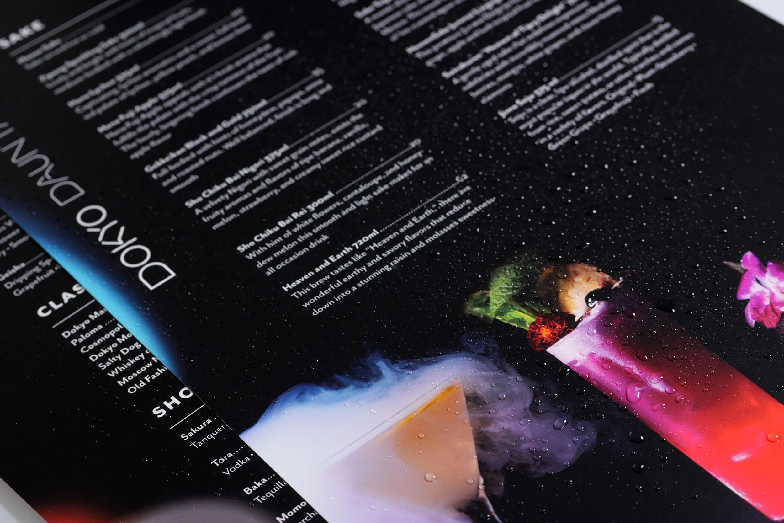 Close-up of a black menu with white text and a colorful cocktail image, covered with water droplets.