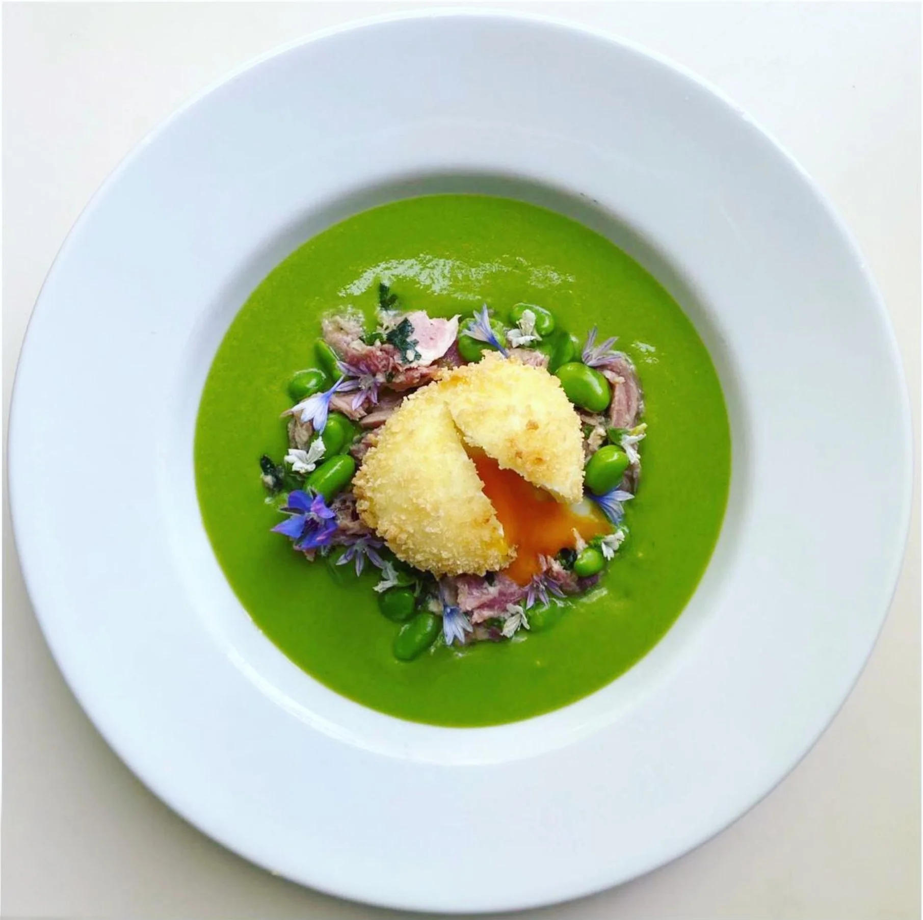 A modern wooden house in a grassy field with mountains in the background.