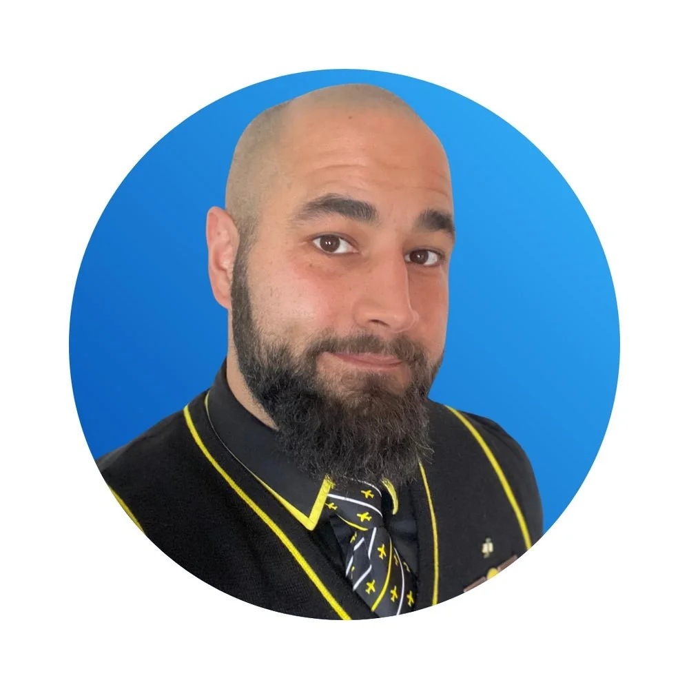 A man with a beard, wearing a black shirt with yellow accents and a tie with yellow and black patterns, posing against a blue circular background.