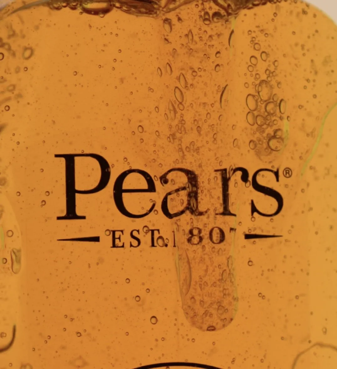 Close-up of a transparent yellow beverage, with bubbles and condensation. Text reads 'Peart's EST. 80'.