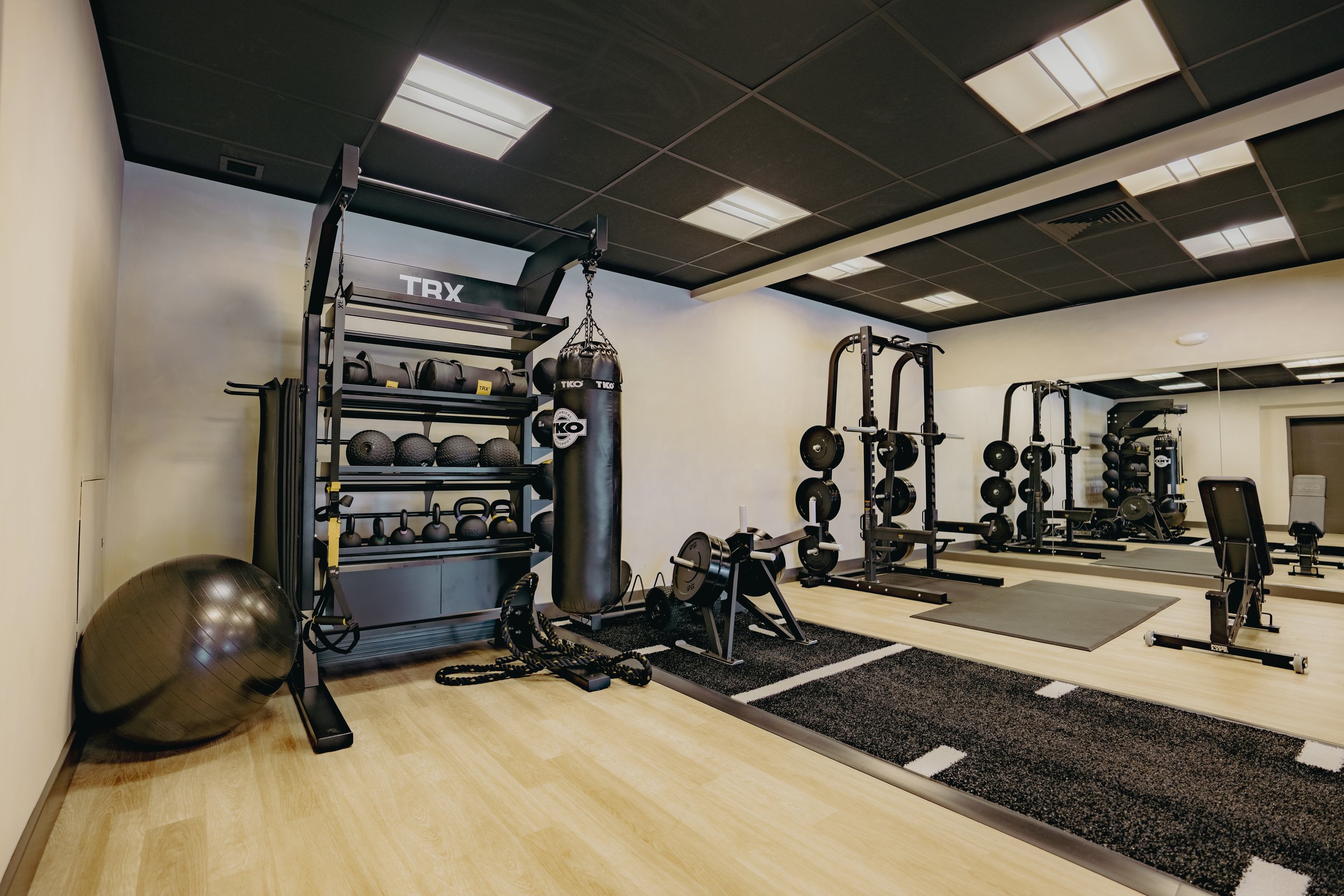 Empty gym with workout equipment including kettlebells, medicine balls, boxing punching bag, weight rack, and exercise mats.