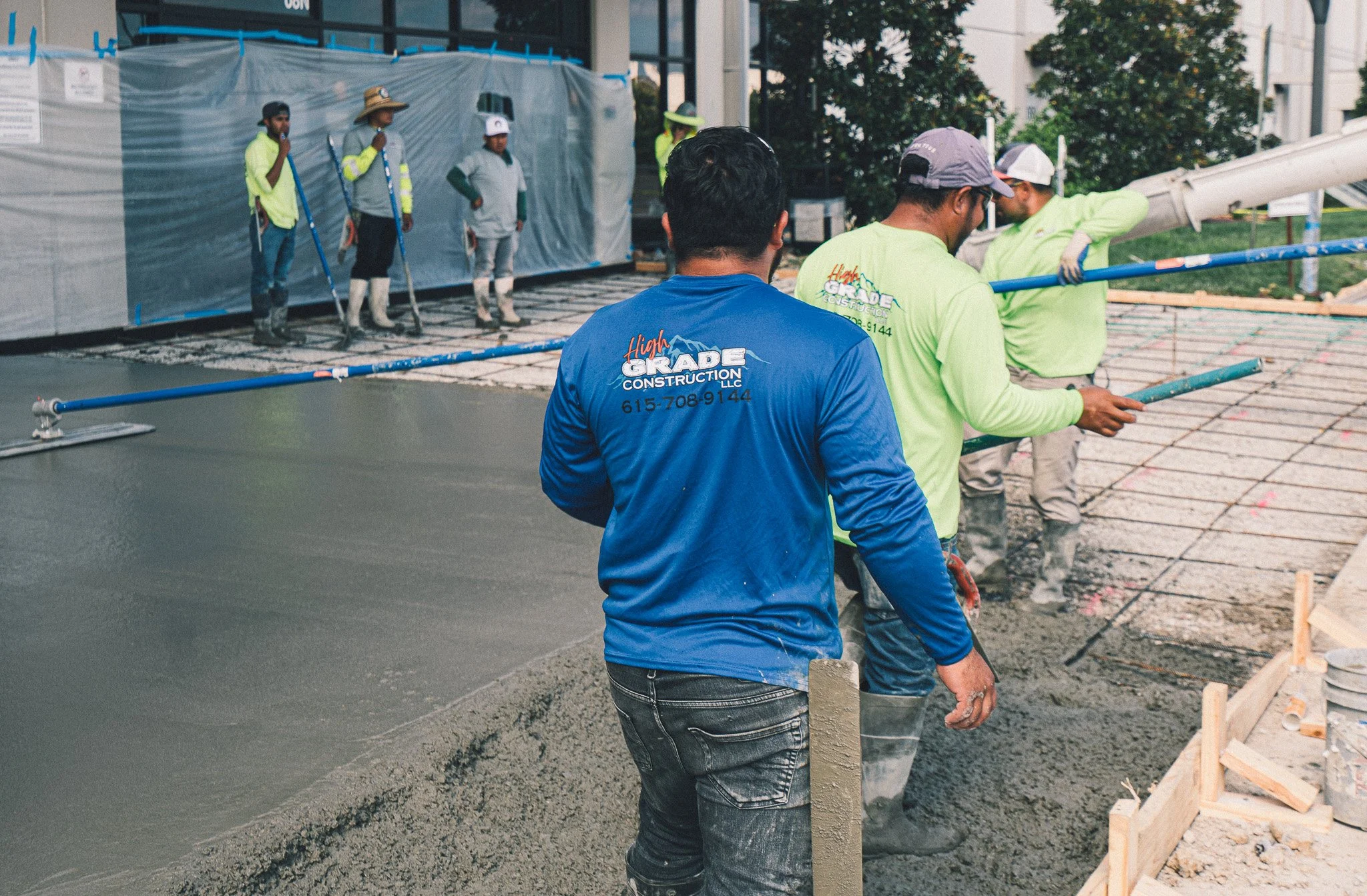 Workers pouring and smoothing concrete on a construction site, with some standing and observing in the background.