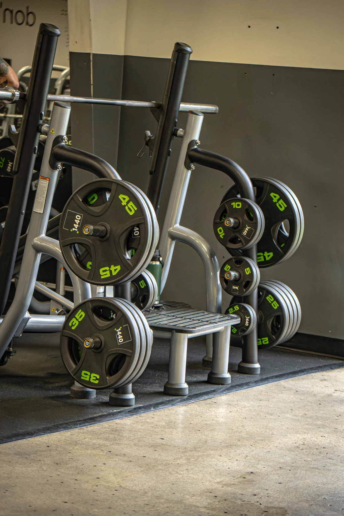 A set of weightlifting barbells and plates arranged on a rack and on the floor in a gym.