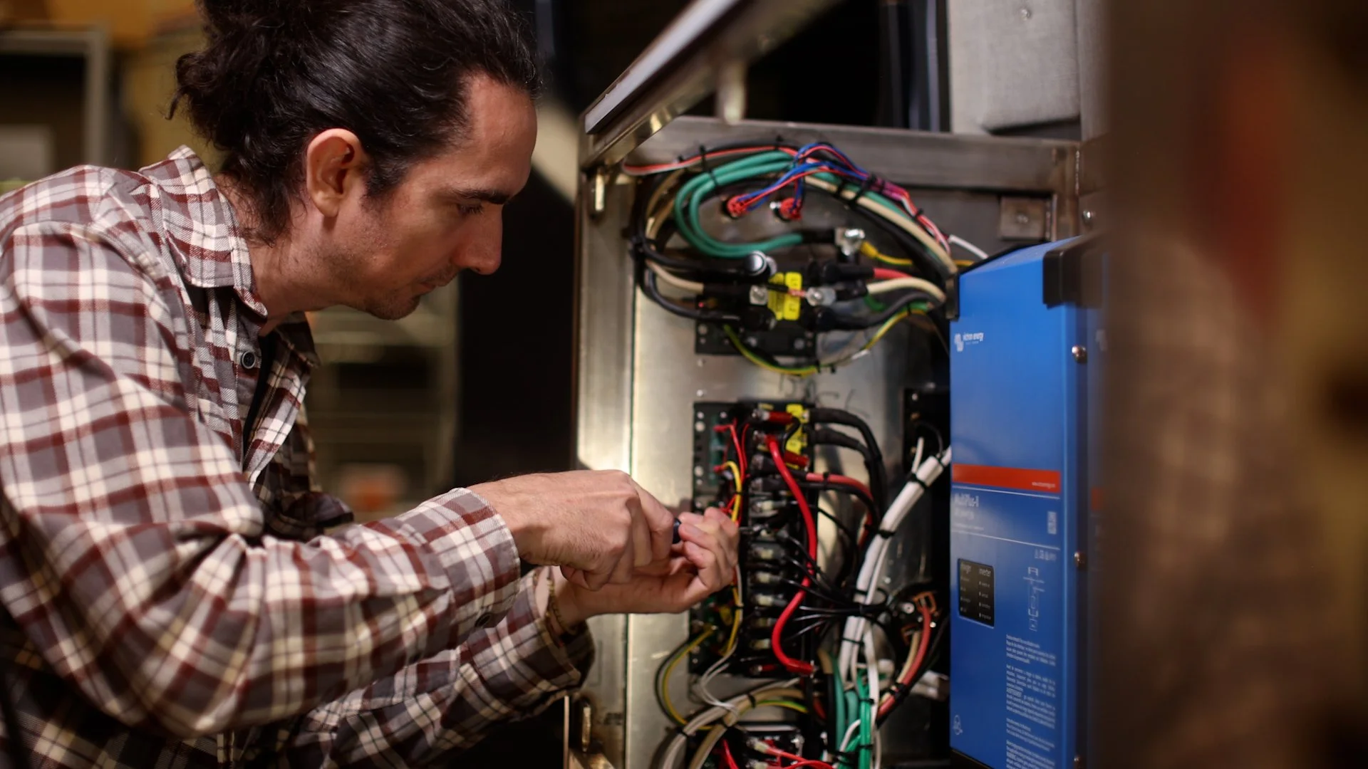 A man in a plaid shirt working on wiring inside an electrical panel or control box.
