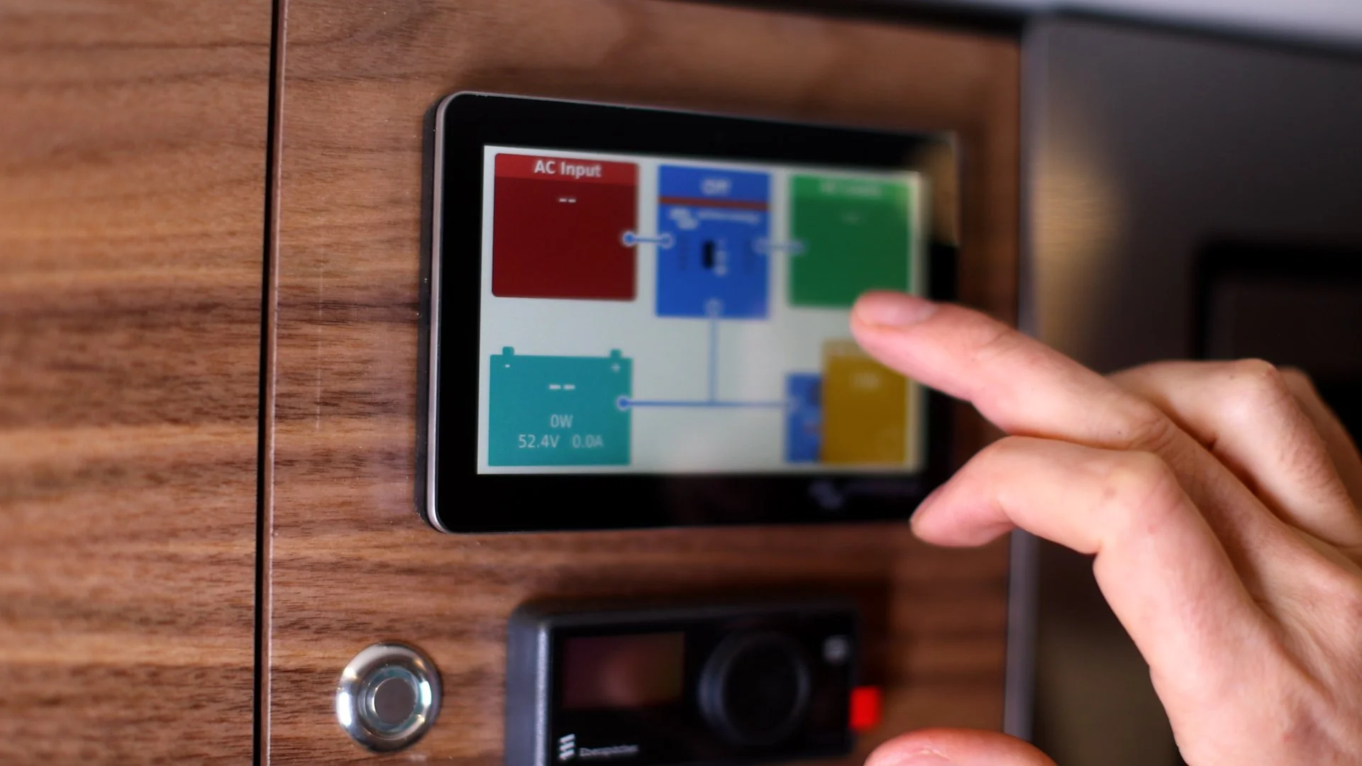 Close-up of a person's hand operating a touchscreen control panel on a wooden surface, with various colored blocks and lines indicating a system diagram.
