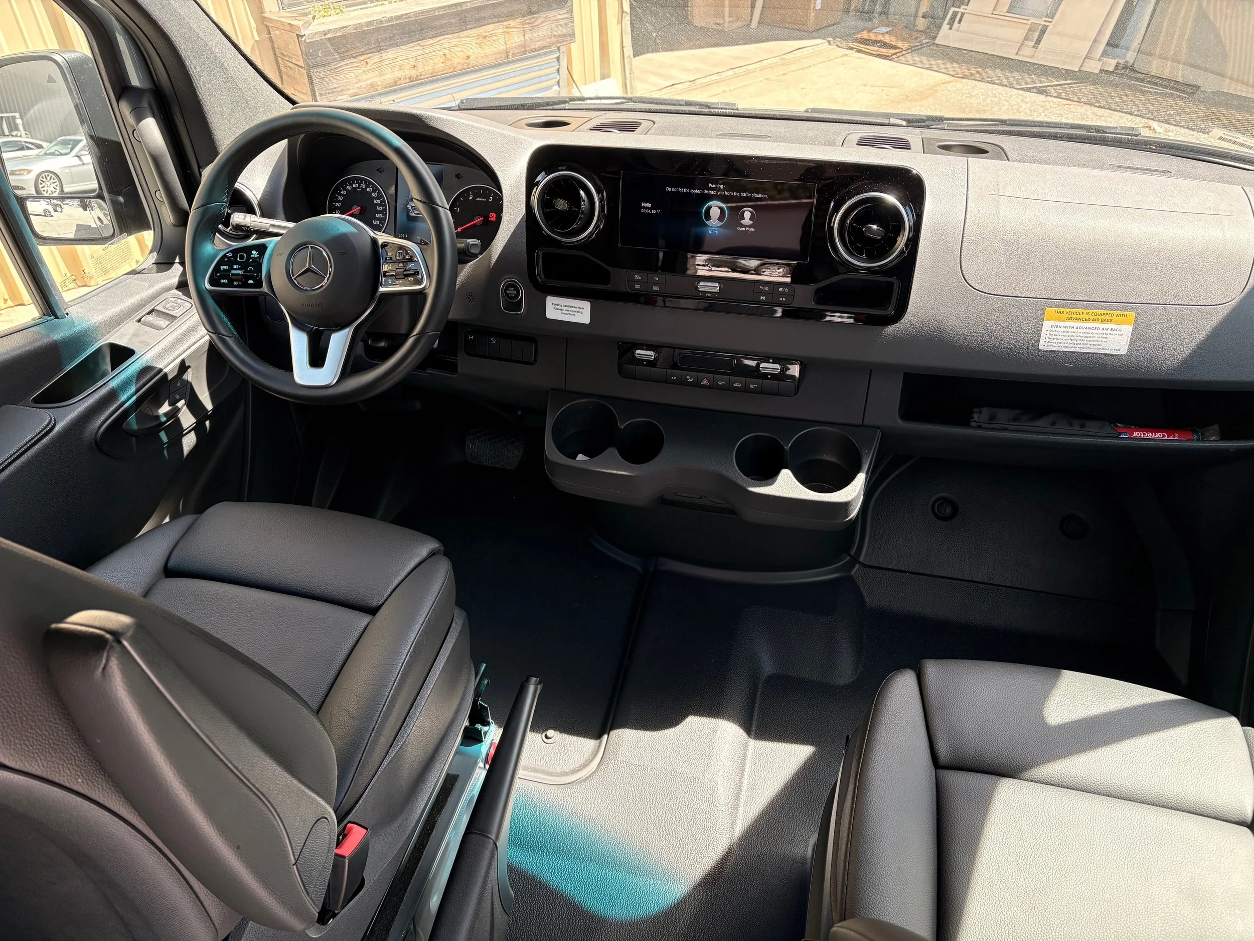 Interior of a Mercedes-Benz van cabin, showing steering wheel, dashboard with digital display, air vents, and control buttons.
