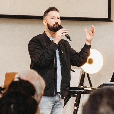 A man with a beard holding a microphone giving a presentation in a room.
