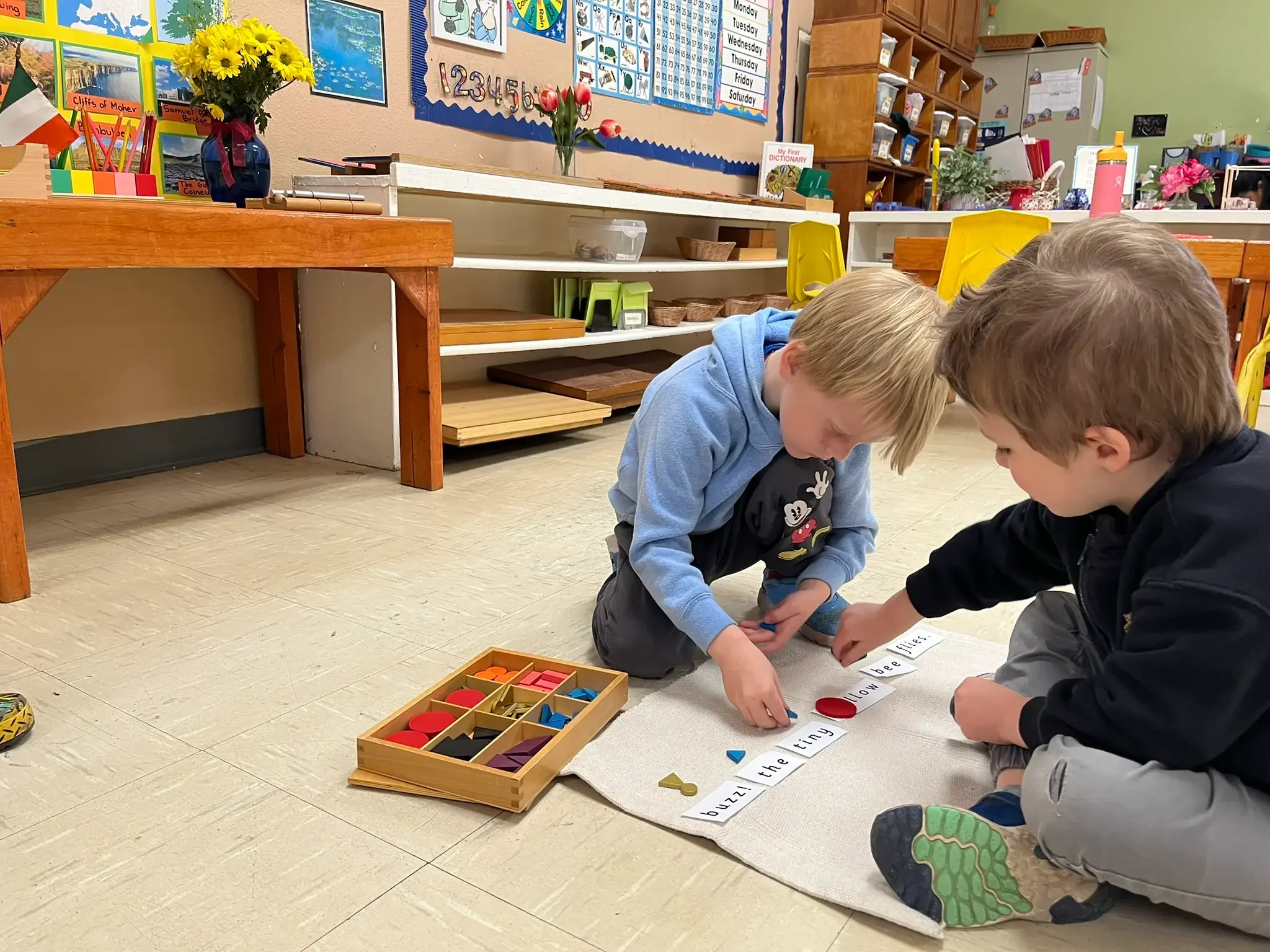 Montessori preschool in Austin, Texas: kindergarten children using grammar symbols and reading words on a mat
